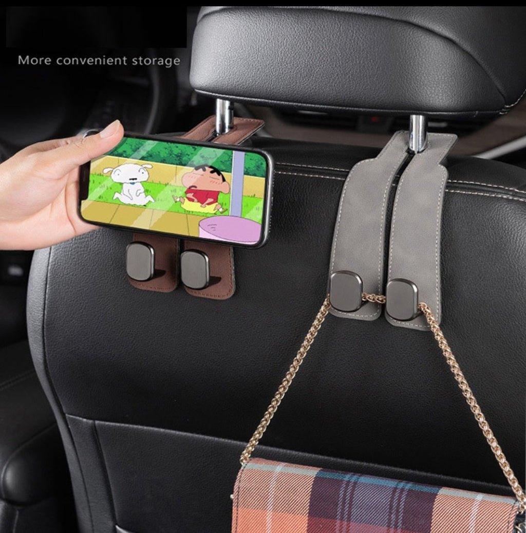 Smartphone held by the brown leather headrest hooks on a car seat back, with a purse hanging from the second hook