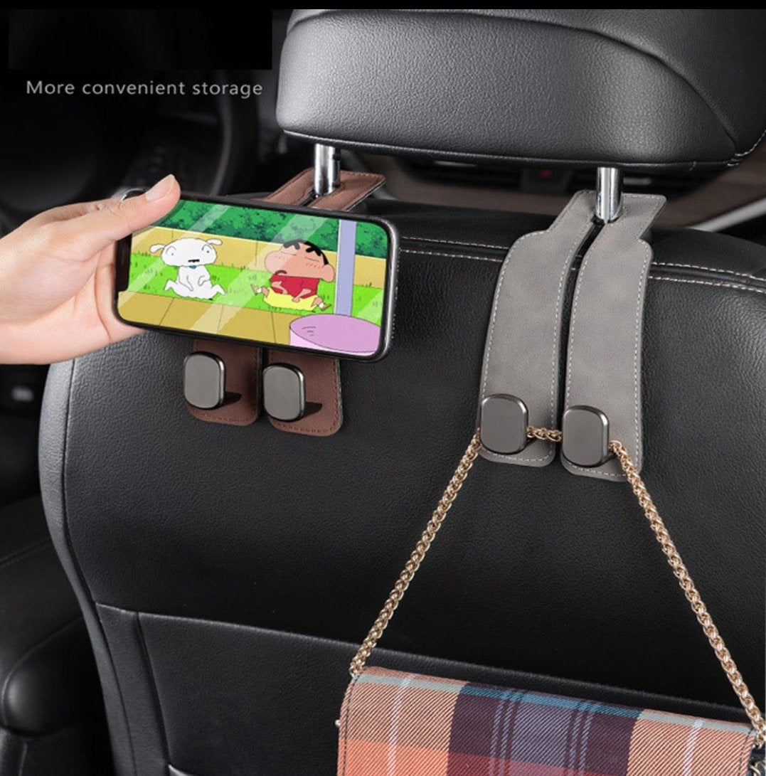 Smartphone held by the brown leather headrest hooks on a car seat back, with a purse hanging from the second hook